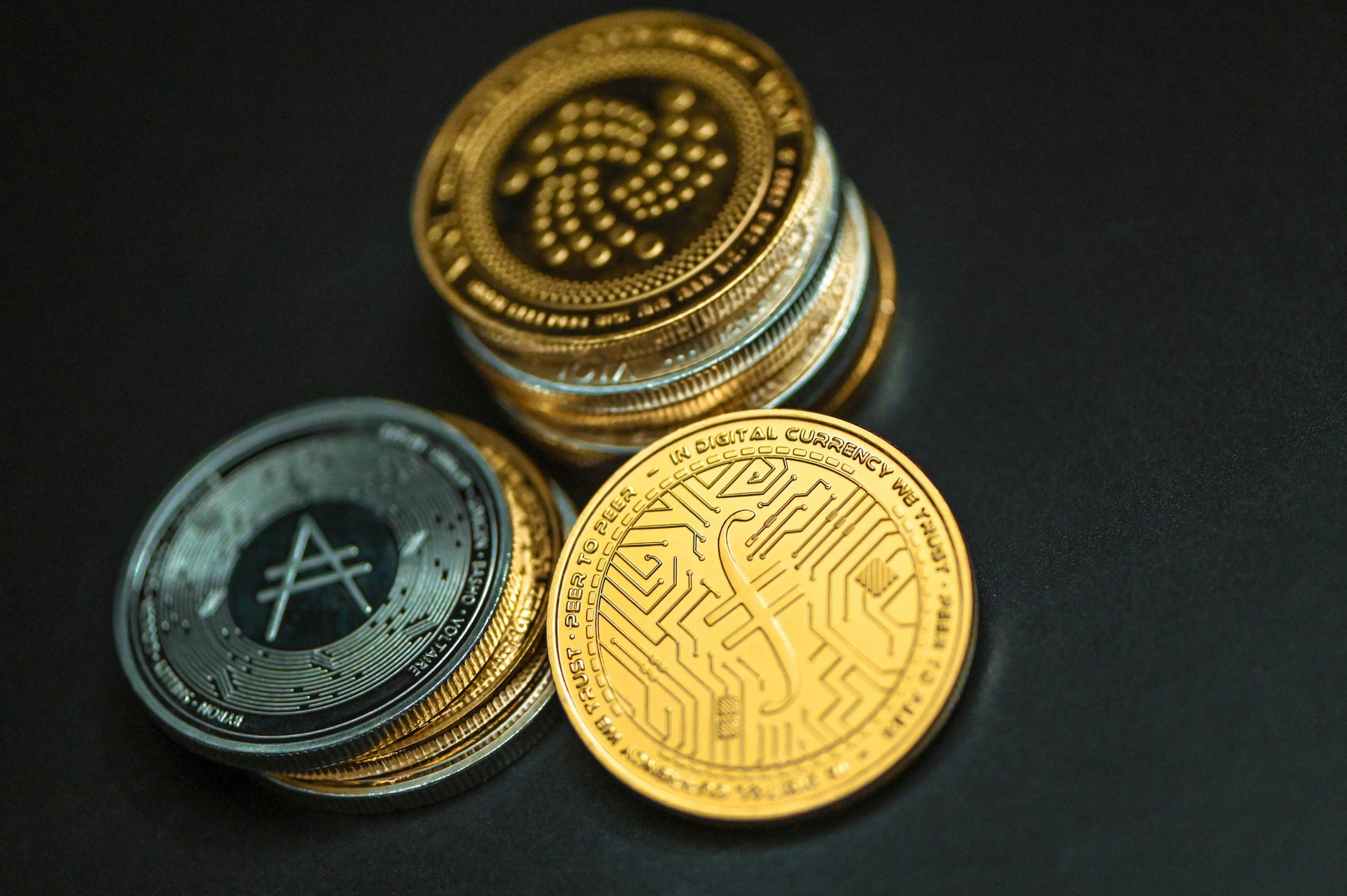 Stapel von Symbolmünzen digitaler Währungen vor schwarzem Hintergrund.