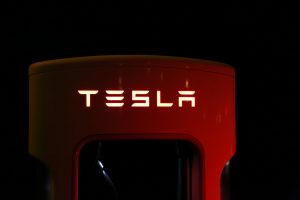 Tesla Schriftzug leuchtend auf rot, vor schwarzem Hintergrund.