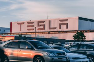 Tesla Schriftzug an Hauswand, vor parkenden Autos.